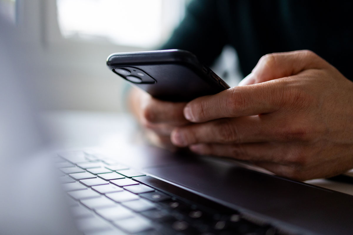 Aufgeschlagenes Laptop, darüber wird ein Smartphone gehalten