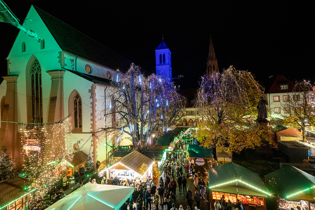 Weihnachtlich beleuchtete Marktstände vor einer Kirche