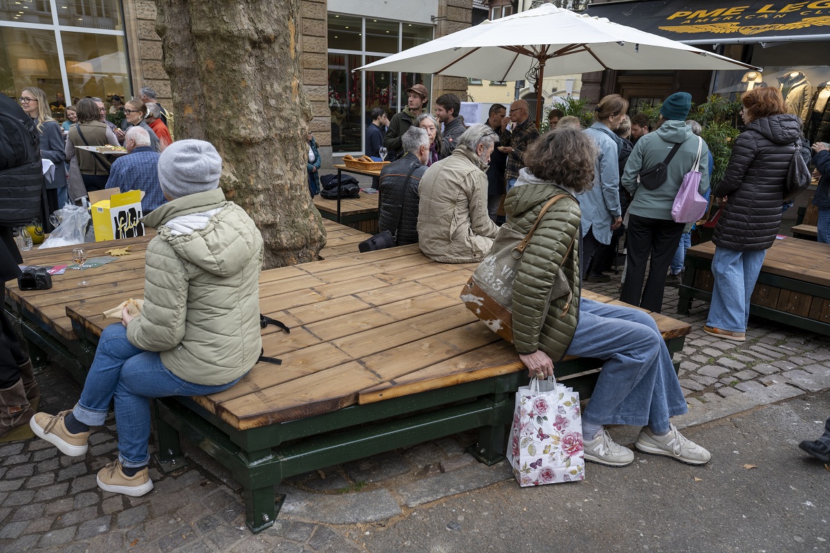 Die neue Grünoase in der Freiburger Innenstadt. Auf dem Holzpodest um einen Baum sitzen Menschen.