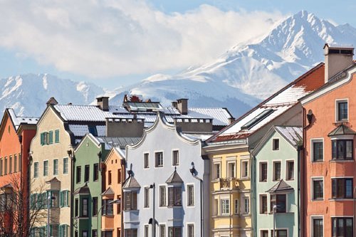 bunte Häuser vor verschneiter Alpen-Kulisse