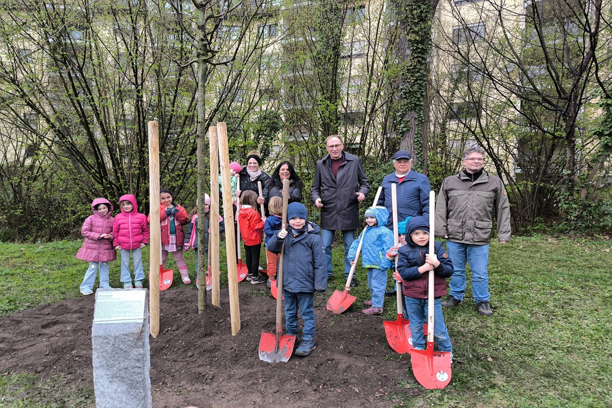 Viele Kinder und Bürgermeister Martin Haag stehen mit Schaufeln und Spaten um den frisch gepflanzten Baum