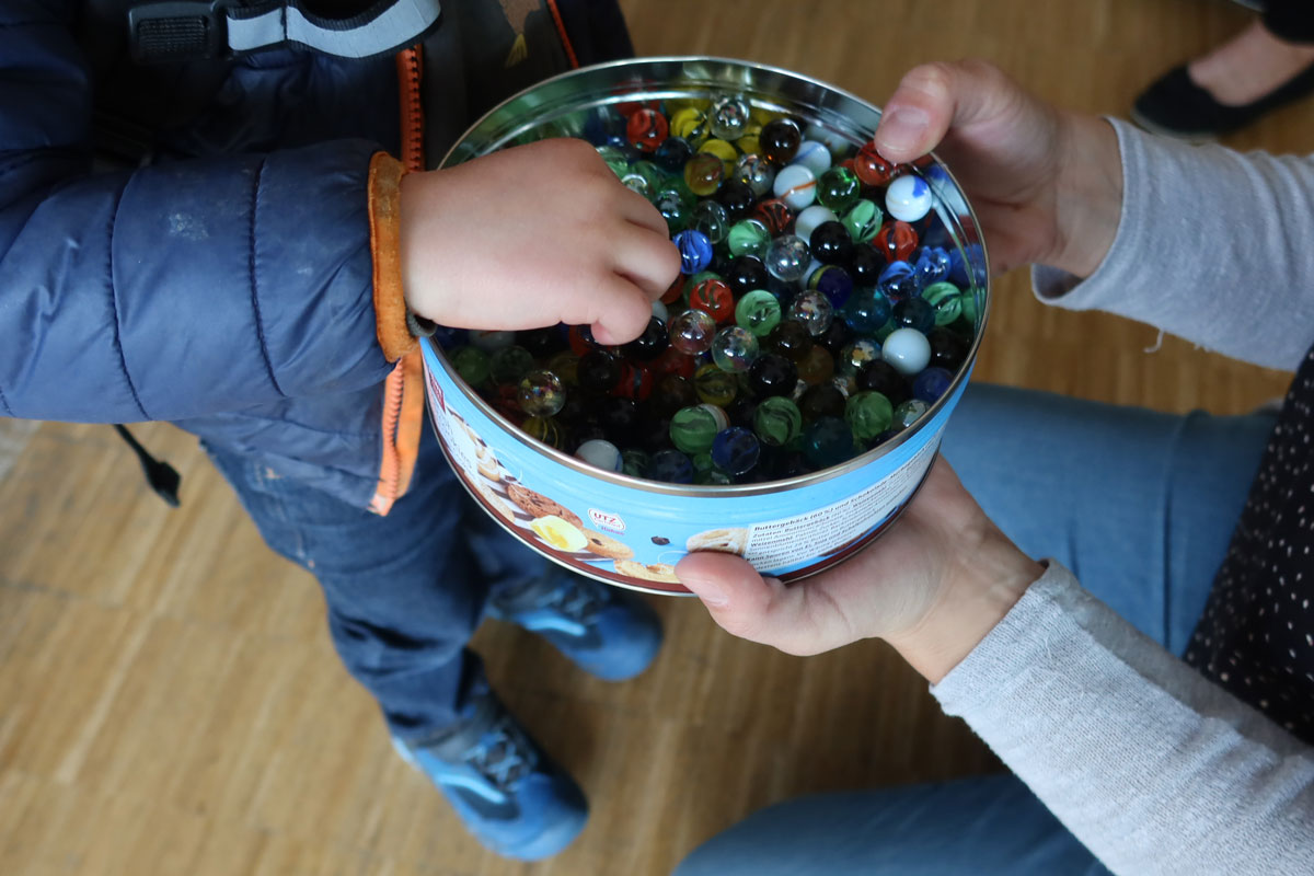 Eine Kind greift in eine Dose mit Murmeln
