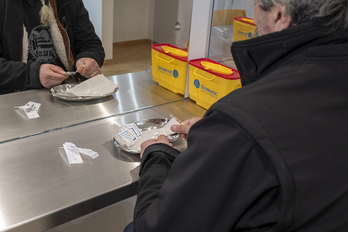 Mann sitzt in Drogenkonsumraum und bereitet sich auf den Konsum vor. Utensilien liegen auf dem Tisch