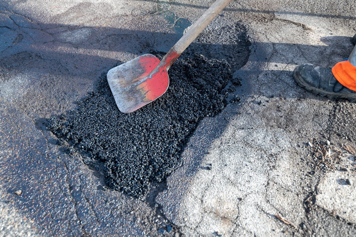Person füllt Schlagloch mit Teer