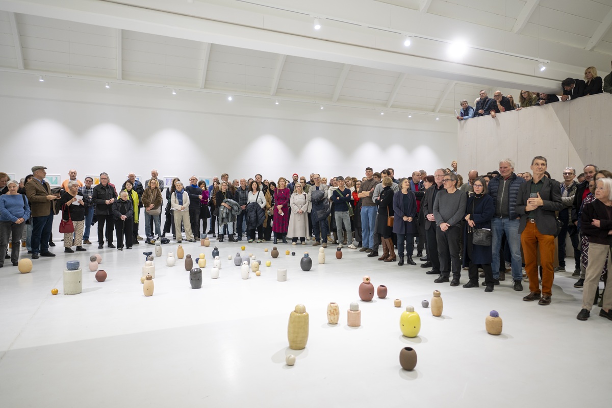 Viele Menschen stehen in einer weißen Halle. Davor viele Keramikkrüge in bunten Farben auf dem Boden angeordnet.