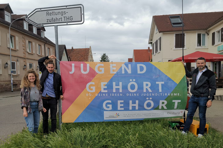 Fachkräfte des Jugendtreffs in Freiburg St. Georgen und der Jugendhilfeplaner der Stadt Freiburg halten plakativ den Banner "Jugend gehört gehört" hoch.