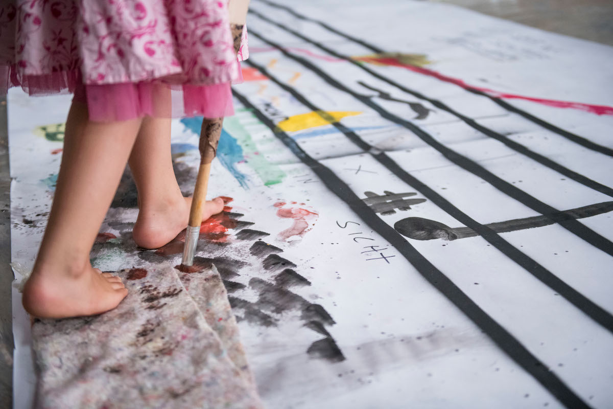 Kind läuft über eine bemalte Plane und malt