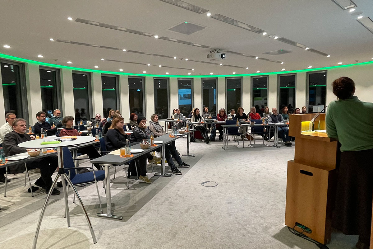 Sitzende Menschen in Veranstaltungsraum mit Redner