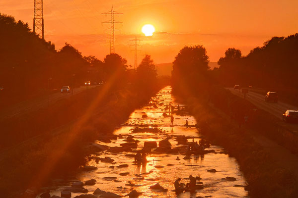 Dreisam mit Menschen, im Hintergrund geht die Sonne unter, orange erleuchteter Himmel