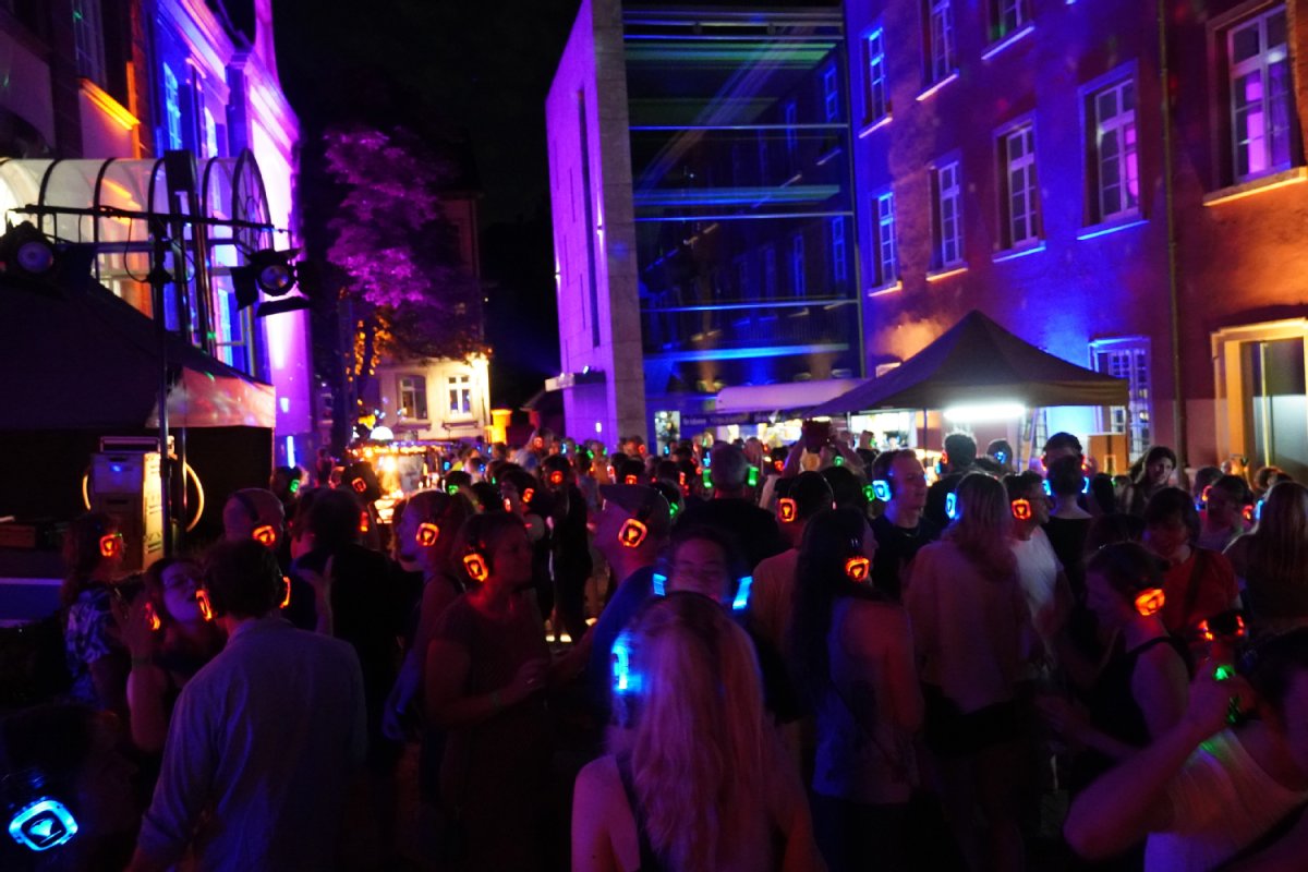 Menschenansammlung nachts, alle tragen Kopfhörer, die an den Seiten leuchten.