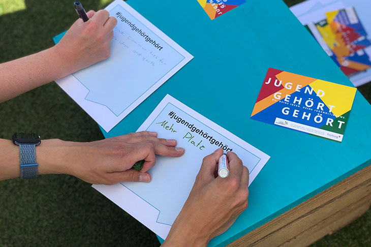 es sind zwei Hände von Jugendlichen sichtbar, die einen Zettel mit dem Hashtag #jugendgehörtgehört beschriften: "mehr Platz"