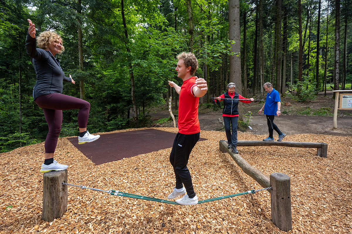 Vier Menschen in Sportkleidung, die im Wald auf Balken balancieren
