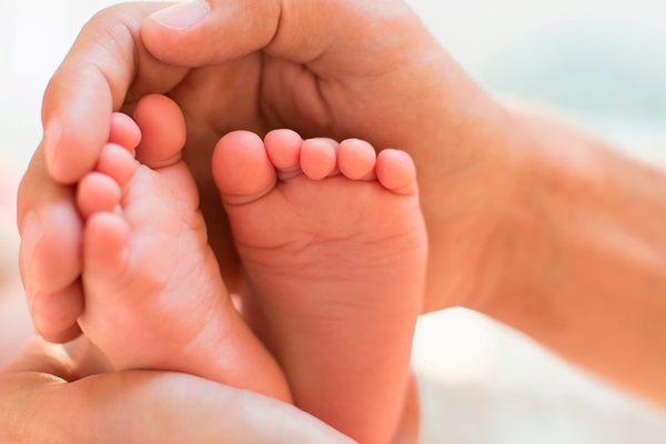 Männerhand umfass zärtlich Babyfüße.