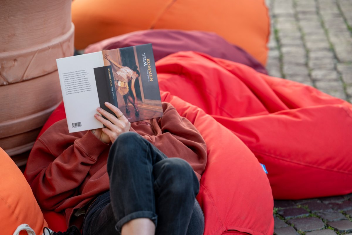 Mensch sitzt auf einem roten Sitzsack und hat ein Buch vorm Gesicht.