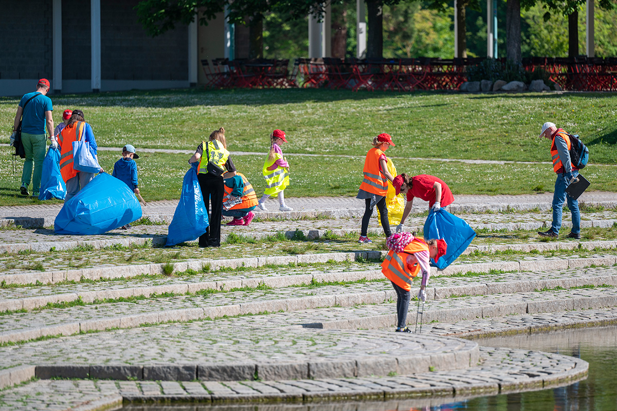 Eine Gruppe Erwachsene und Kinder in Warnwesten beim Müllsammeln an einem See