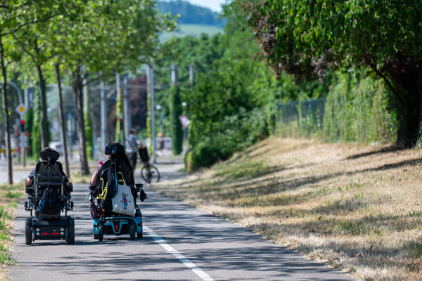 Zwei Personen in Rollstuhl auf Gehweg