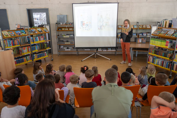 Eine Frau liest einer Gruppe von Kindern in einer Bibliothek aus einem Buch vor.