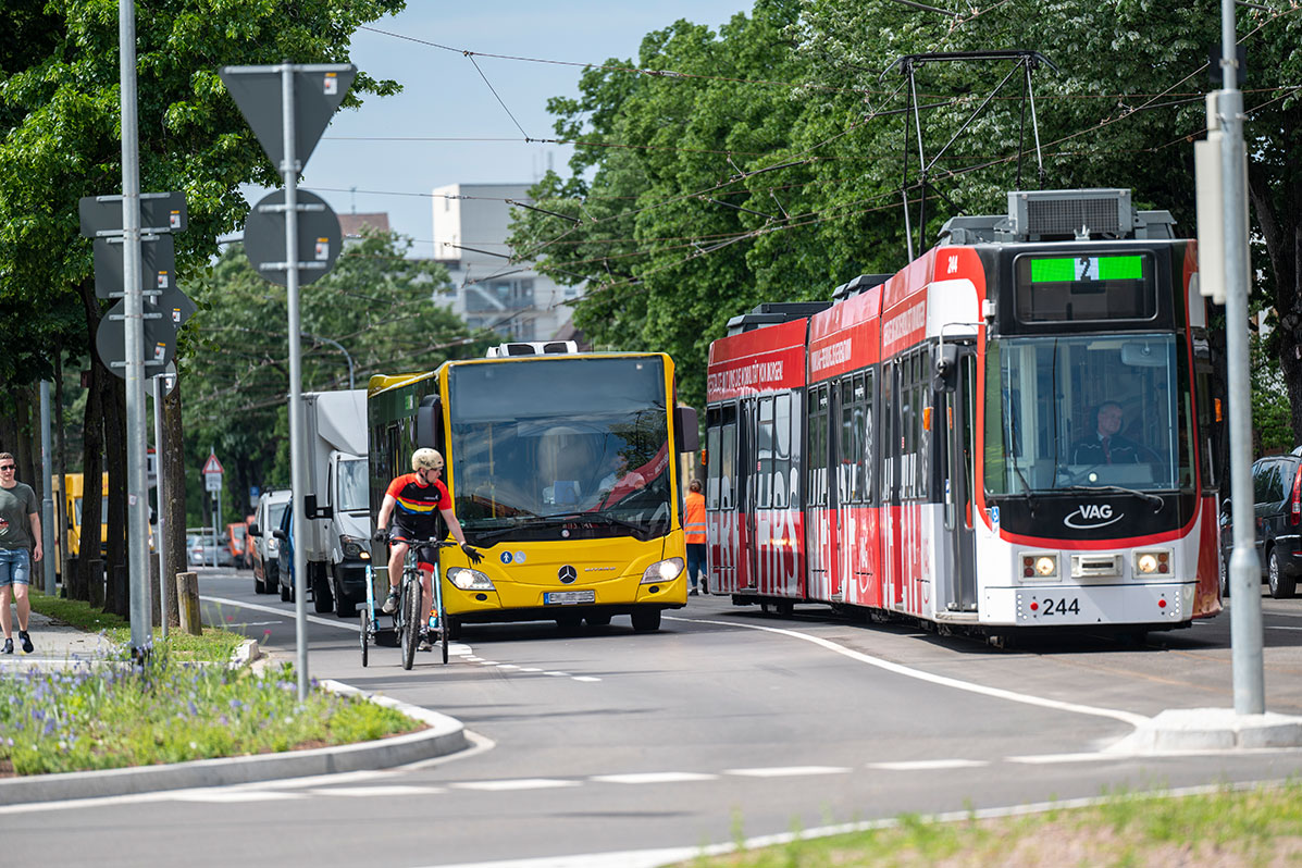 Kreuzung mit gelbem Bus, roter Straßenbahn und Fahrradfahrer mit Kinderanhänger