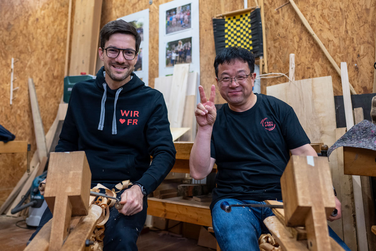 Zwei Personen sitzen auf einem Schniedesel und bearbeiten Holz