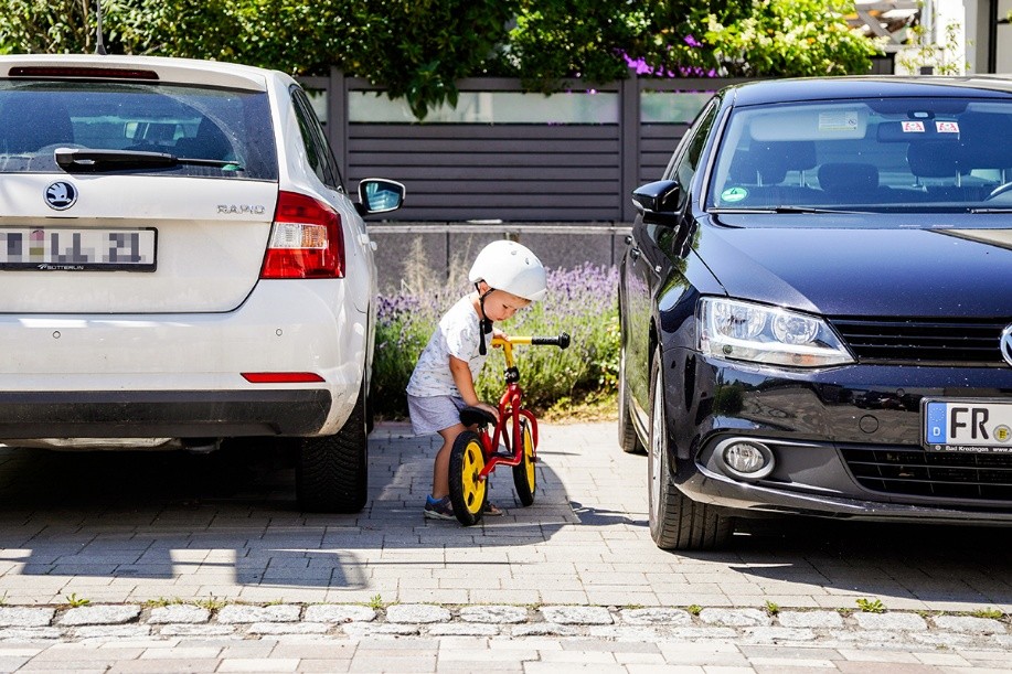Foto: David Laukart Kleines Kind parkt sein Laufrad zwischen zwei parkenden Autos