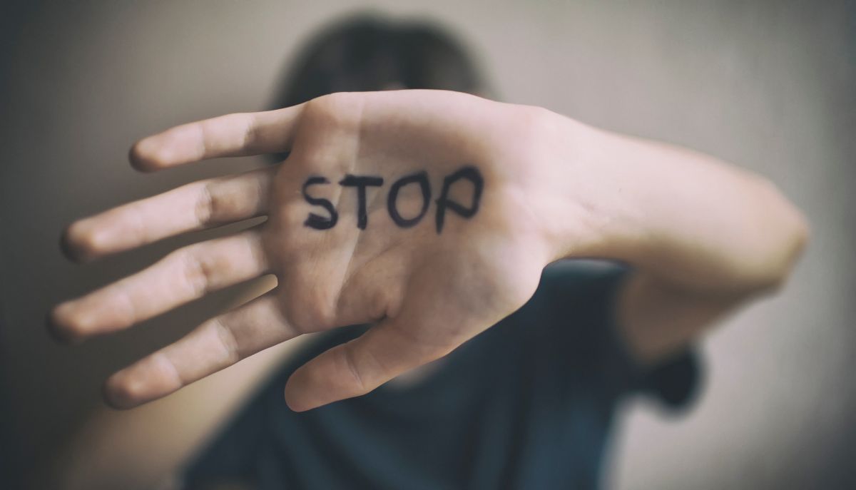 Frau hält Hand vor das Gesicht mit Schriftzug "Stop".