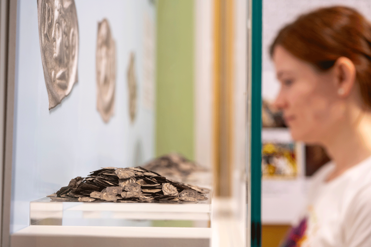 Frau steht vor Ausstellungsvitrine in der Münzen sind