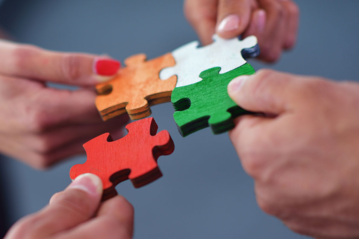 Foto: .shock/istock.com Vier Hände halten vier verschiedenfarbige Puzzleteile aneinander.