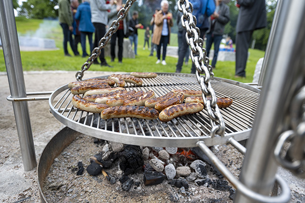 Grillrost mit Würstchen, im Hintergrund Menschen