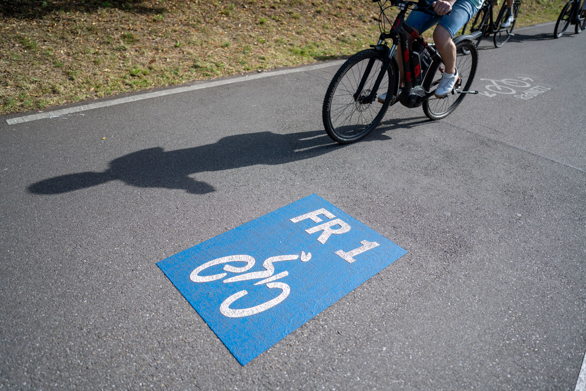 Person sitzt auf Fahrrad und fährt, auf dem Boden ein FR 1 Logo