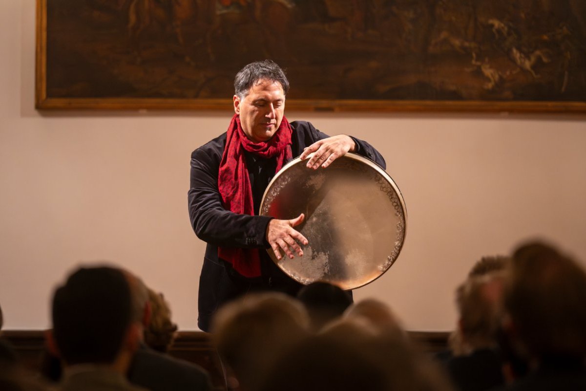 Murat Coşkun im roten Schal auf einer Bühne mit einer Rahmentrommel