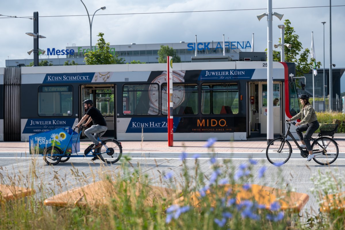 An der Straßenbahn-Haltestelle "Messe". Zwei Fahrräder im Vordergrund, darunter ein Lastenrad, im Hintergrund eine Straßenbahn der Linie 4.