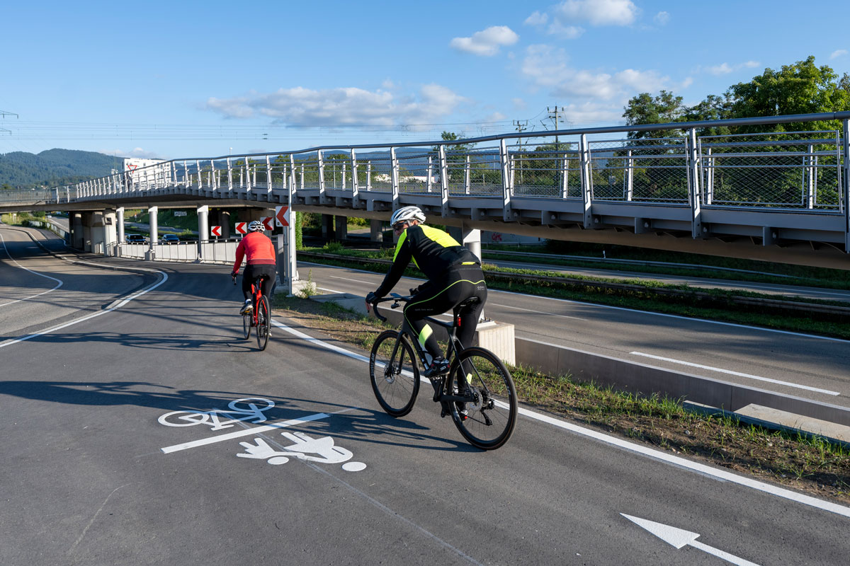 Zwei Radfahrer auf einem Radweg, im Hintergrund die Radwegrampe
