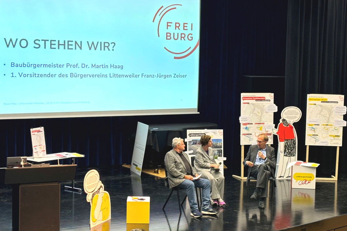 Drei Redner*innen im Gespräch auf einer Bühne