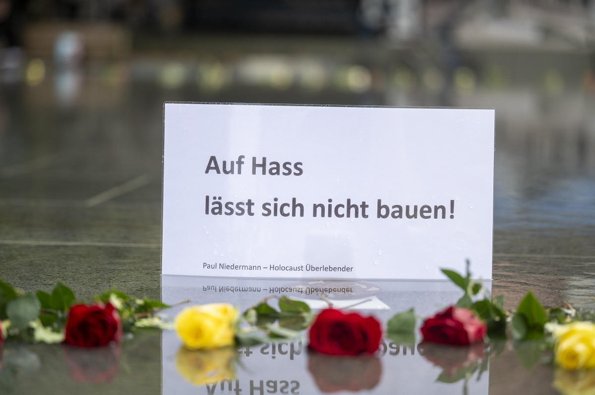 Zettel mit Aufschrift: "Auf Hass lässt sich nicht bauen", davor sind Rosen niedergelegt