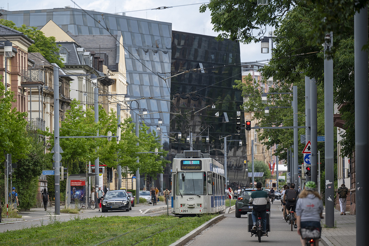 Autos, Radfahrende und eine Straßenbahn vor der Universitätsbibliothek Freiburg