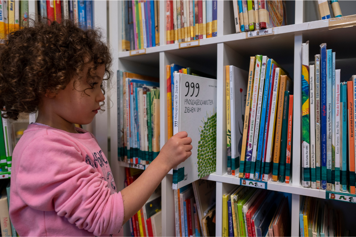 Ein Mädchen zieht ein Buch aus einem vollen Bücherregal.