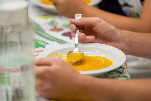 Kinderhände löffeln Kürbissuppe aus einem Teller.