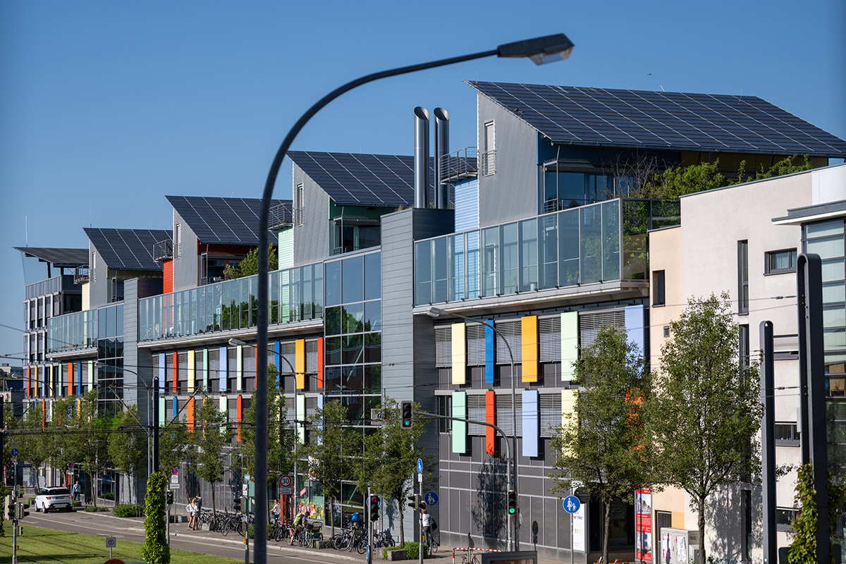 Häauserfassade bei Tag, viel beglast und auf den Zwischendächern begrünt; Photovoltaik-Anlagen auf den Dächern.