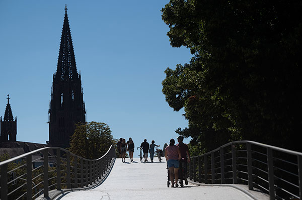 Mehrere Menschen gehen zu Fuß über die Brücke, die die Innenstadt mit dem Stadtgarten verbindet.