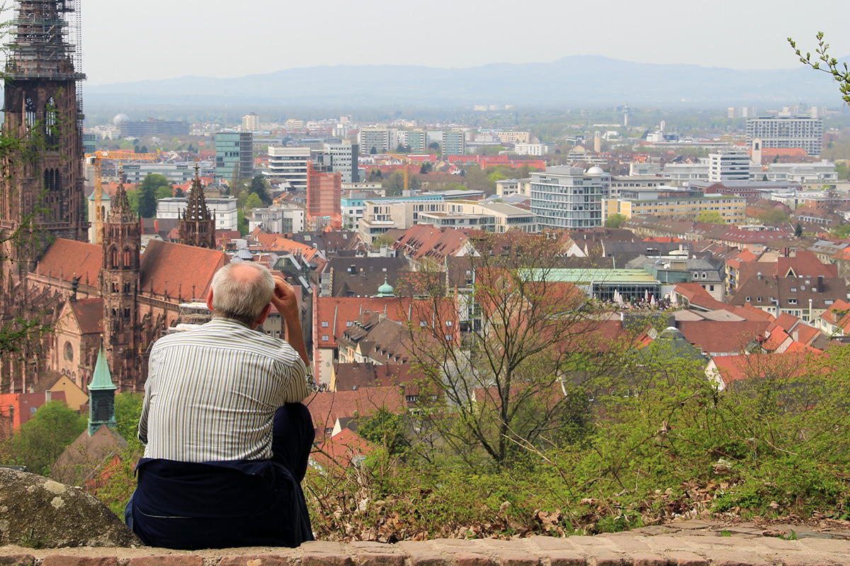 Ein älterer Mann sitzt auf einer Mauer am Kanonenplatz und schaut auf die Innenstadt