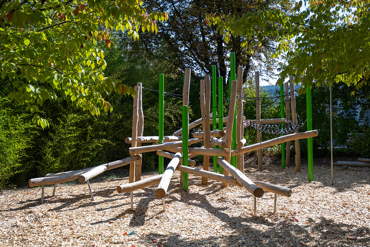 Klettergerüst auf Rindenmulch-Untergrund; Viele naturnahe Baumstämme horizontal und vertikal angeordnet, dazu schwarze Seile und Netze.