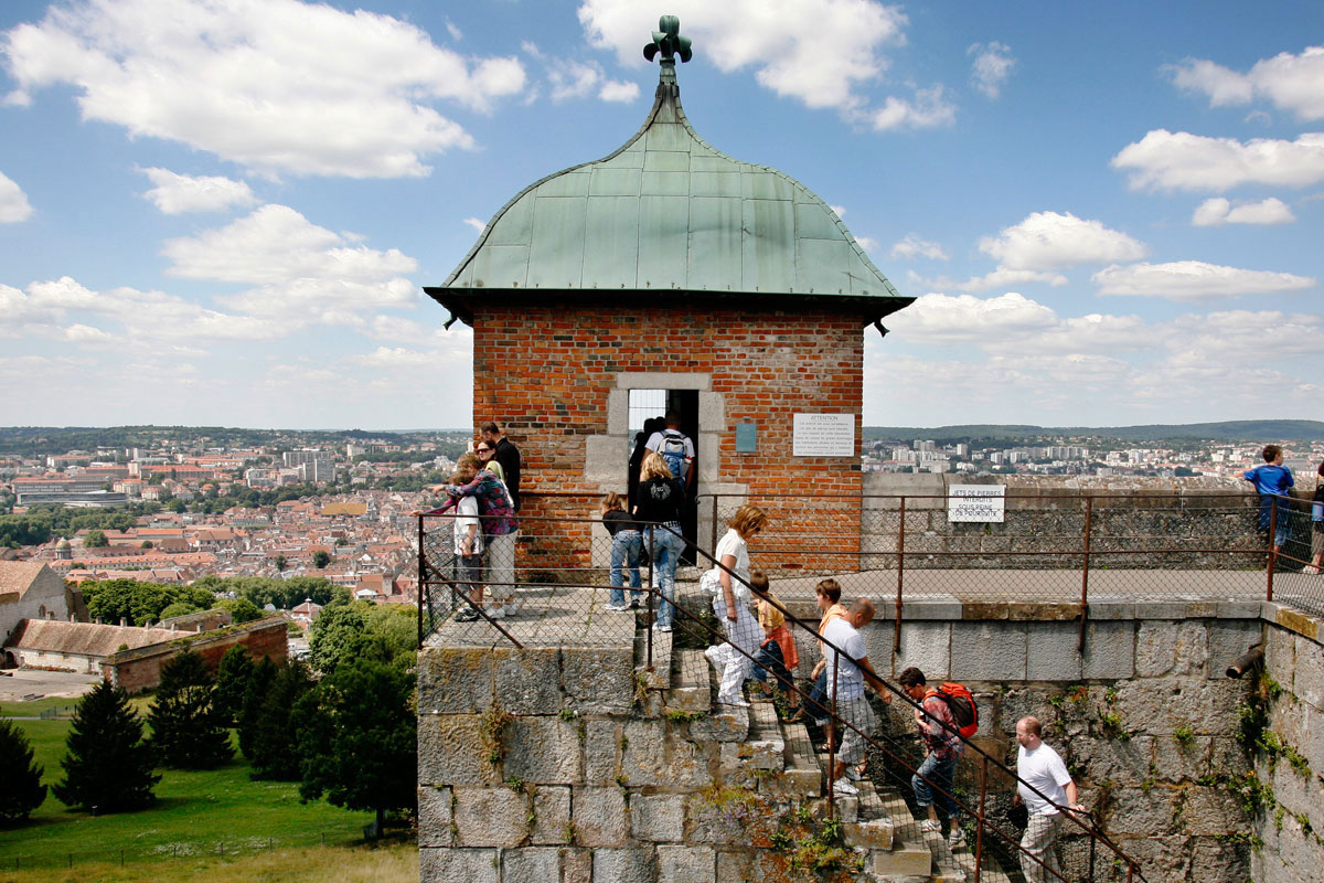 Menschen laufen eine Treppe zu einem Turm nach oben, im Hintergrund eine Stadt
