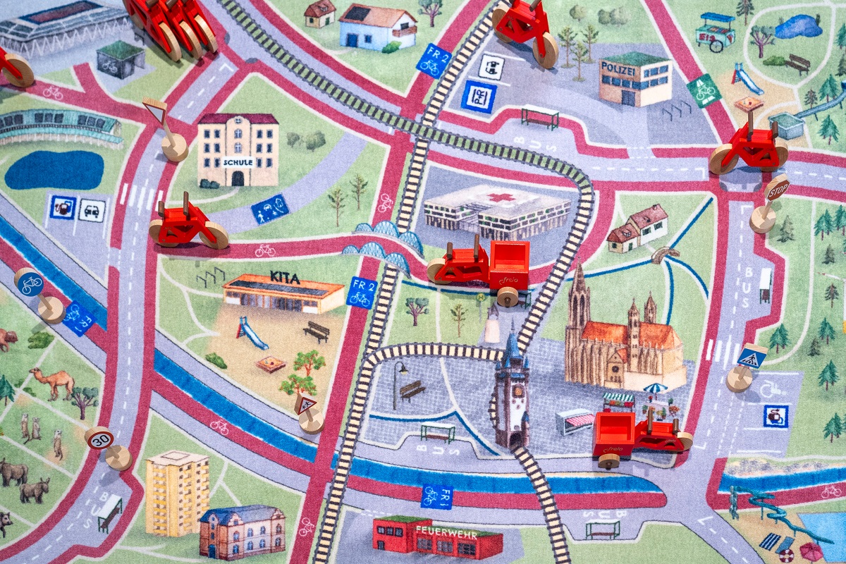 Freiburger Spielteppich mit Stadtion, Münster und anderen Gebäuden und kleinen Spielzeugfahrzeugen