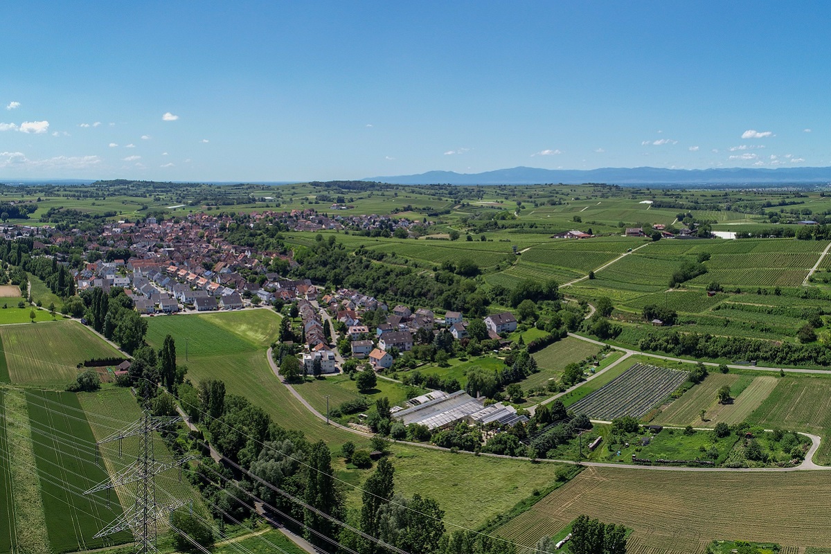 Landschaftsbild mit landwirtschaftlichen Flächen, Baumreihen an Wegen und einem Ort in de Ferne 
