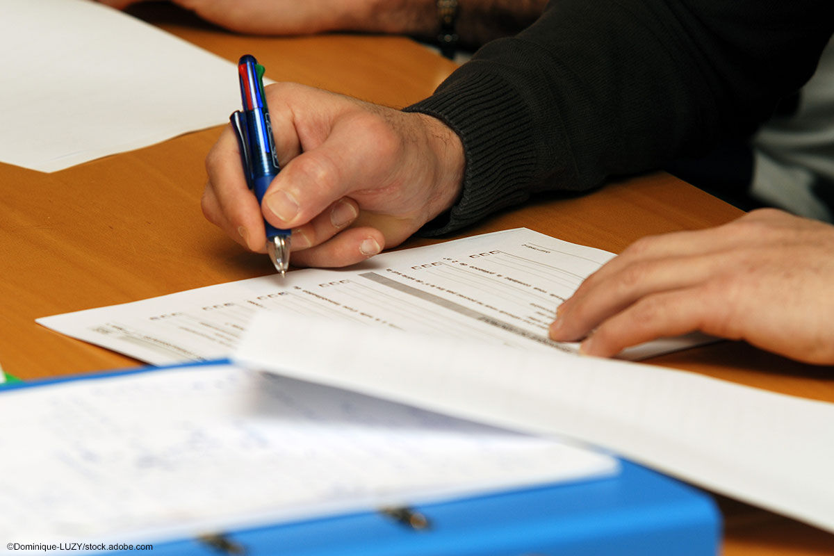 Hand mit Kugelschreiber, die einen Antrag ausfüllt.