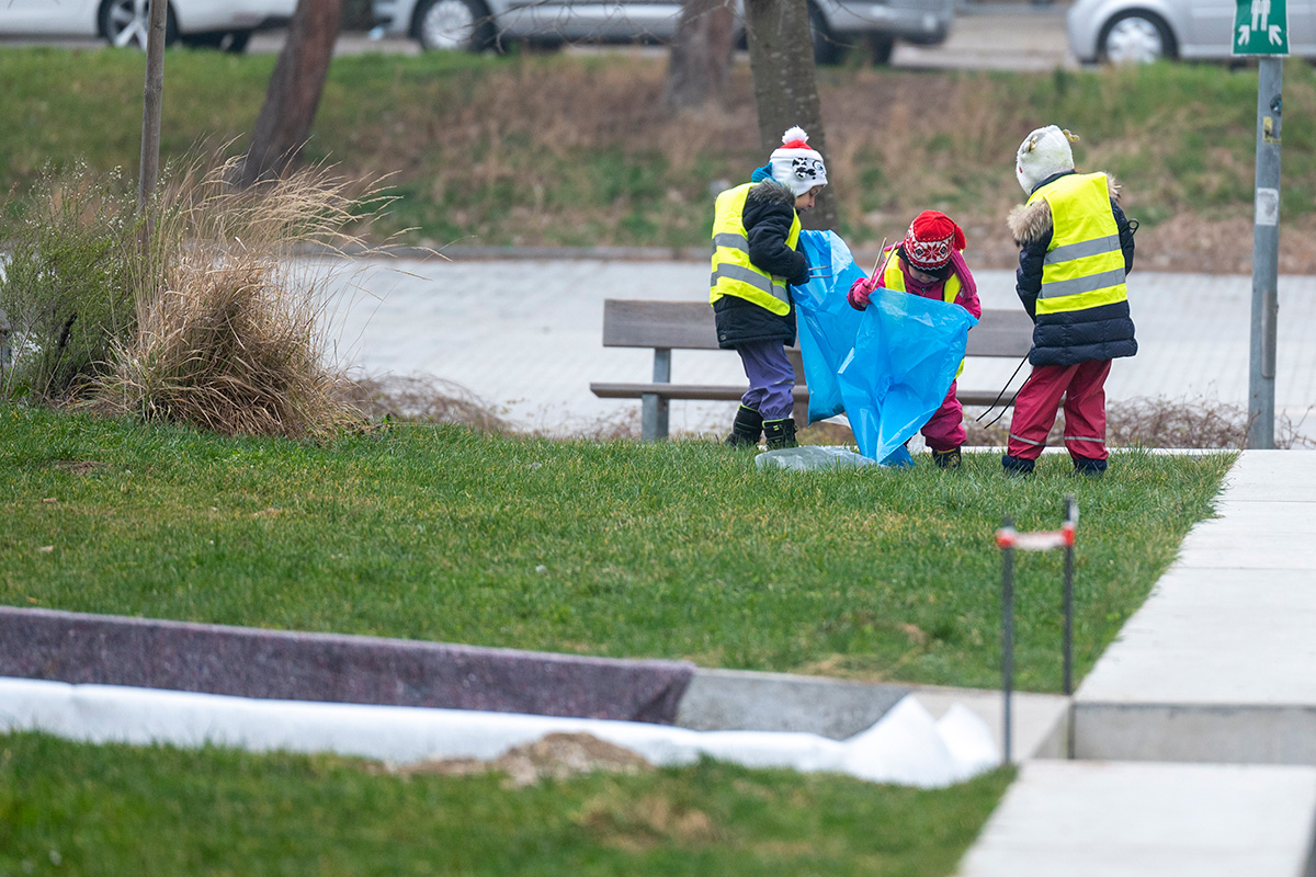 Drei Kinder in Warnwesten beim Müllsammeln an einer Parkbank