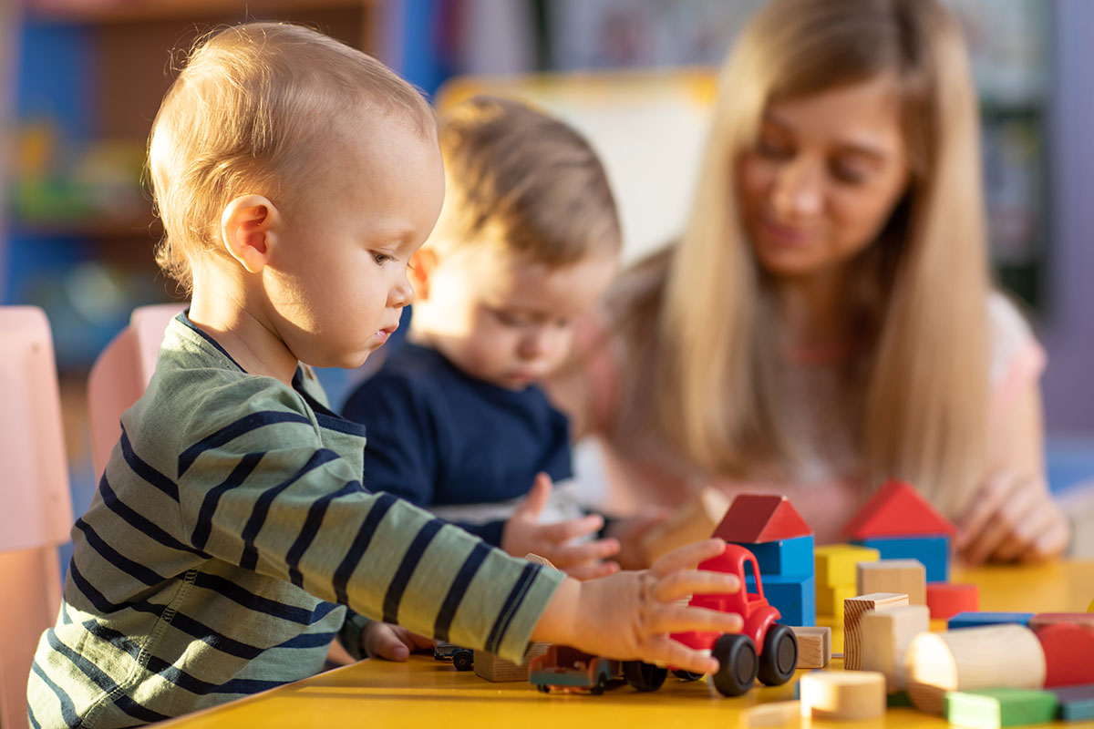 Zwei kleine Kinder und eine Erzieherin spielen mit Bauklötzen.
