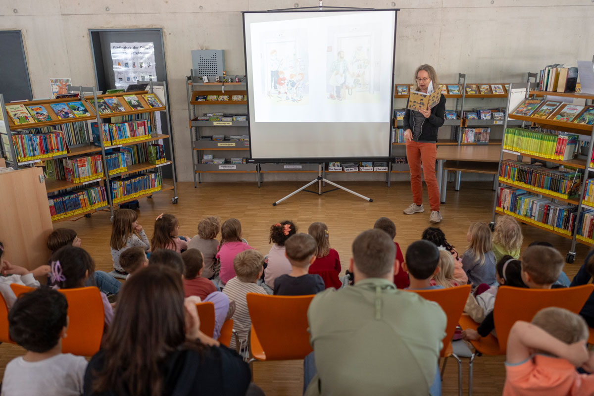 Eine Frau liest einer Gruppe von Kindern in einer Bibliothek aus einem Buch vor.