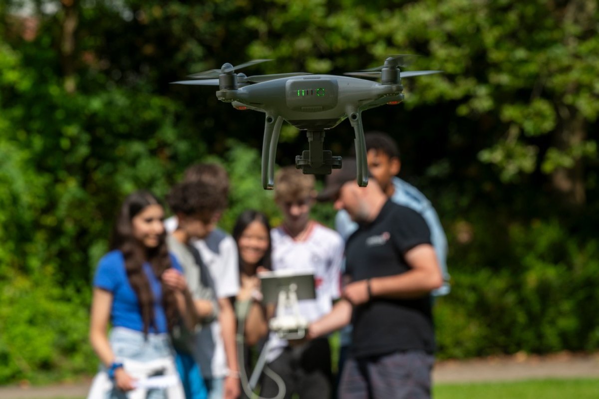 Eine Drohne im Vordergrund, die von Jugendlichen gesteuert wird.
