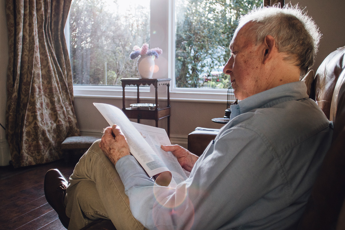 Älterer Mann in einem Sessel, der eine Zeitschrift liest.